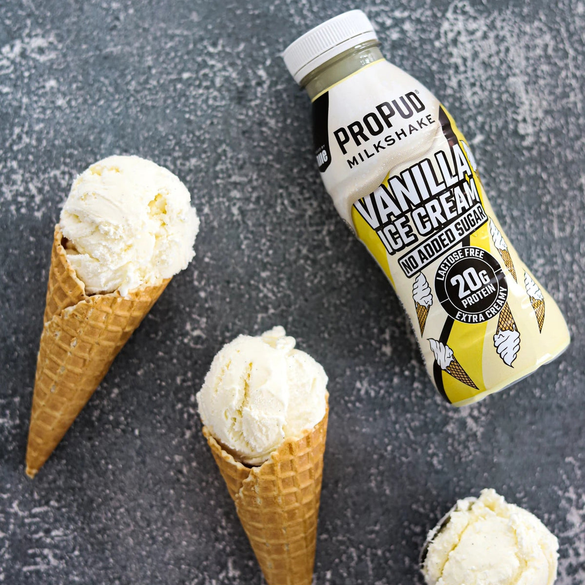 A bottle of Propud Milkshake Vanilla Cinnamon Smoothie Syrup placed on a dark textured surface next to three vanilla ice cream scoops in waffle cones.